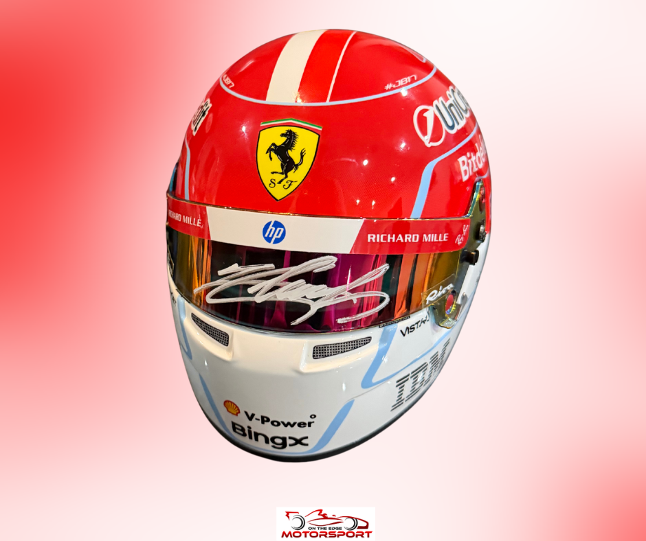 An autographed red and white Ferrari racing helmet with sponsor logos including HP, Vissler, and Quiksilver, displayed against a pink gradient background.