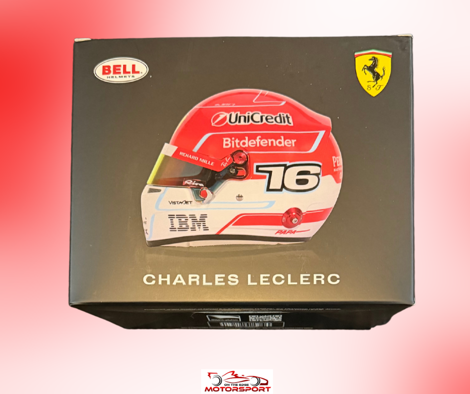 A boxed collectible model or figurine of racing driver Charles Leclerc, shown from the front on a red-to-pink gradient background. The packaging is black with a printed image of Leclerc's red, white, and black Ferrari helmet, plus visible Bell, Ferrari, UniCredit, Bitdefender, and IBM logos.